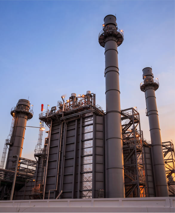 Modern industrial power plant facility with tall chimneys and complex infrastructure at sunset.